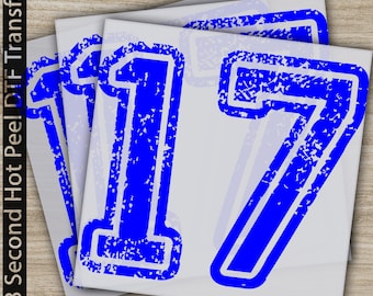 Puede incluir: Una pila de hojas de transferencia cuadradas blancas con el número 17 grande y en negrita impreso en un color azul vibrante. El número 17 tiene una apariencia texturizada y desgastada con un borde azul grueso y un centro blanco sobre una superficie.