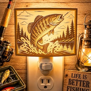 May include: A rectangular plug-in night light featuring an illuminated engraved design of a fish jumping out of water with a forest background. The light is plugged into a wall outlet and emits a warm glow, showcasing detailed line art of the scene.