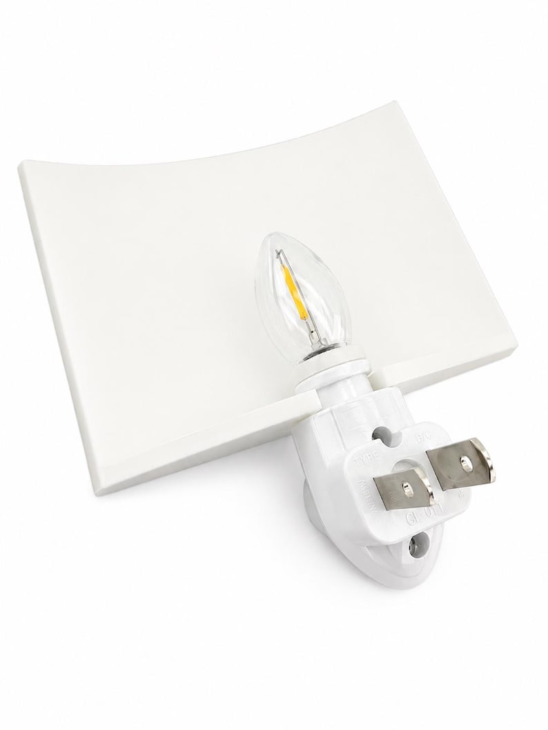 Pode incluir: Uma luz noturna branca de tomada com uma c&uacute;pula retangular curva e uma l&acirc;mpada LED transparente em formato de vela com um filamento amarelo vis&iacute;vel. A base inclui um plugue el&eacute;trico de dois pinos para instala&ccedil;&atilde;o direta na parede.