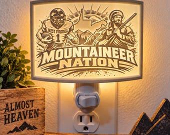 Könnte beinhalten: Ein rechteckiges Nachtlicht für die Steckdose mit einer hinterleuchteten Grafik eines Footballspielers und eines Bergsteigers sowie dem Schriftzug Mountaineer Nation. Das Design zeigt einen Umriss von West Virginia und Bergsilhouetten.