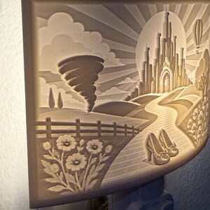 Pode incluir: Uma luz noturna retangular com um relevo de uma paisagem fant&aacute;stica. A cena inclui um tornado, um grande castelo, uma estrada de tijolos sinuosa, um par de sapatos de salto alto, flores em primeiro plano e um bal&atilde;o de ar quente no c&eacute;u.