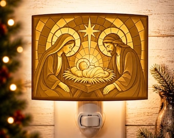 Könnte beinhalten: Ein rechteckiges Nachtlicht mit einer warm beleuchteten Krippenszene. Das Motiv zeigt Maria und Josef, die neben dem Jesuskind in einer Krippe knien, vor einem Hintergrund im Buntglasstil mit einem zentralen Stern über den Figuren.