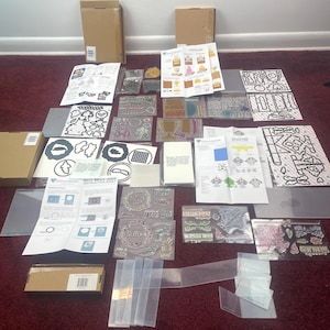 May include: A collection of craft supplies for card making and scrapbooking. The supplies include clear stamps, die cuts, stencils, and embellishments. The supplies are arranged on a red carpet.
