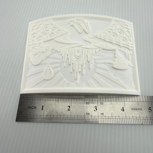 Pode incluir: Um molde de silicone branco retangular com um design em relevo de um lustre central, padr&otilde;es florais e raios de sol. Uma r&eacute;gua de a&ccedil;o inoxid&aacute;vel est&aacute; posicionada na borda inferior, mostrando uma largura de 12,7 cm para o molde.
