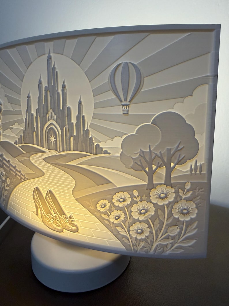 May include: A curved, illuminated white lamp featuring a relief carving of a castle, a hot air balloon, a brick path, a pair of high-heeled shoes, and flowers. The scene is backlit, creating a warm glow that highlights the intricate details.