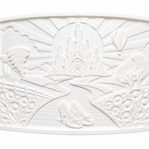 Pode incluir: Uma placa retangular de relevo branco apresentando uma cena detalhada em relevo de um castelo, uma estrada sinuosa, um par de sapatos de salto alto em primeiro plano, um bal&atilde;o de ar quente, um tornado e elementos florais sob um c&eacute;u radiante.