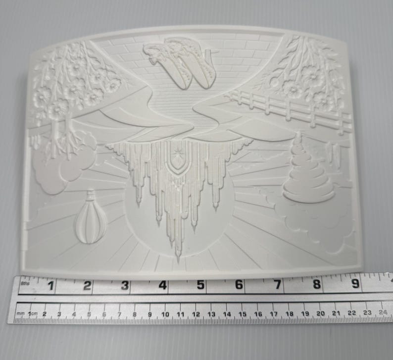 May include: A white rectangular silicone mold featuring an embossed landscape design with a hot air balloon, flowers, a fence, and a central castle-like structure. A ruler placed at the bottom shows the mold width is approximately 9.5 inches.