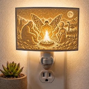 May include: A rectangular night light with a detailed relief scene of a campfire with a Bigfoot, a moth-like creature, and an alien. The background features a forest, mountains, and a full moon. The light plugs into a standard wall outlet.
