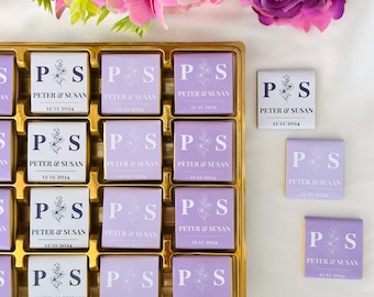 Può includere: Un vassoio dorato riempito con quadratini di cioccolato avvolti in carta viola chiaro. Ogni pezzo presenta le lettere P e S, un disegno floreale a linee e il testo PETER & SUSAN 12/12/2024. Tre pezzi aggiuntivi sono posti accanto al vassoio.
