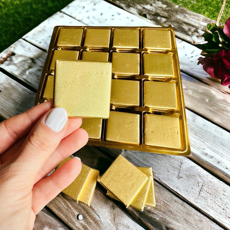 May include: A gold chocolate bar tray with individual squares of gold foil wrapped chocolate. Some of the squares are loose and sitting on a wooden surface.