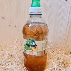 Könnte beinhalten: Eine durchsichtige Plastikflasche Volvic Tee mit Pfirsichgeschmack. Die Flasche hat einen grünen Deckel und ein weißes Etikett mit dem Volvic-Logo und dem Text "Savoir Pêche" und "Sans Sucres Ajoutés".