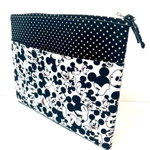 May include: A black and white zippered pouch featuring a Mickey Mouse pattern. The top section is black with white polka dots. The main body of the pouch has a repeating pattern of Mickey Mouse's face and body.
