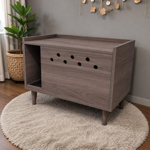 May include: A rectangular pet enclosure cabinet with a dark gray wood grain finish, supported by four tapered legs. The front panel features a series of circular ventilation holes arranged in a pattern, with an open side compartment on the left.