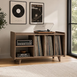 May include: A wooden media console with four vertical storage compartments for vinyl records, a shelf for an audio receiver, and a top surface holding a turntable. The console features tapered legs and a natural wood grain finish.
