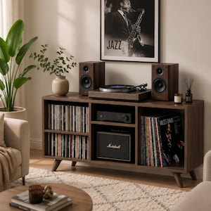 May include: A dark wood media console with tapered legs, featuring open shelving filled with vinyl records, a turntable on top, two speakers, a central amplifier, and a black Marshall speaker. A framed jazz poster hangs on the wall above the unit.