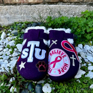 May include: A pair of purple fuzzy slippers with various patches, including a paw print, a star, a pink ribbon, and the text "Believe, Fight, Hope".