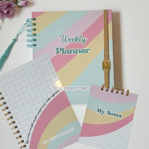 Puede incluir: Un conjunto de tres cuadernos de espiral de colores pastel con diseños de arcoíris. El cuaderno más grande dice "Weekly Planner" y tiene un cierre de cinta dorada. El cuaderno mediano tiene un patrón de cuadrícula y dice "God makes everything good, perfect, and at the right time" y "CAROLINA CORDON". El cuaderno más pequeño dice "My Notes".