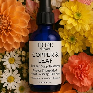 May include: A blue glass bottle of HOPE skincare Copper & Leaf hair and scalp treatment, surrounded by orange, yellow, and white flowers. The label includes product information and the text "2 oz / 60 ml".