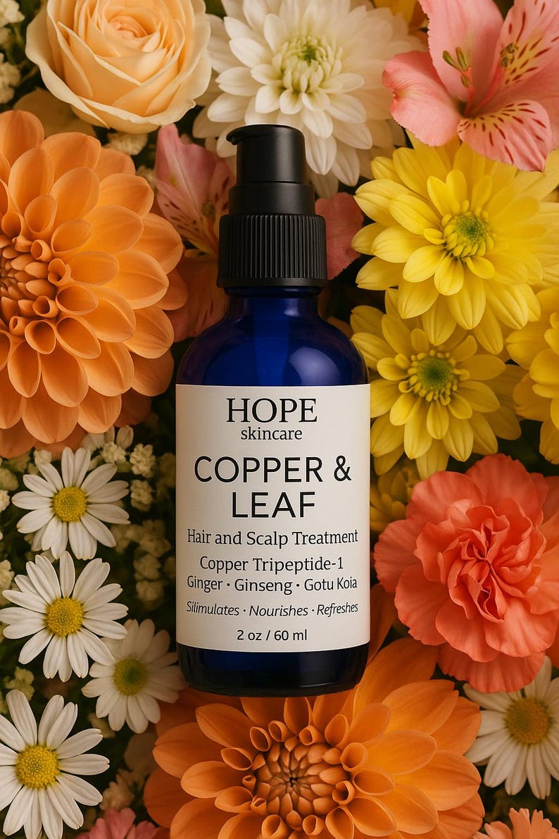 May include: A blue glass bottle of HOPE skincare Copper & Leaf hair and scalp treatment, surrounded by orange, yellow, and white flowers. The label includes product information and the text "2 oz / 60 ml".