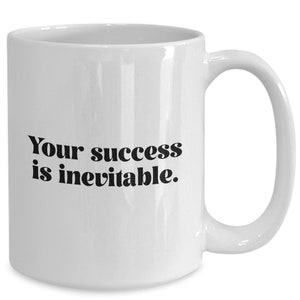 May include: White ceramic coffee mug with black text that reads "Your success is inevitable."