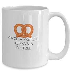 May include: White ceramic coffee mug with a brown pretzel graphic and the text "Once a pretzel, always a pretzel".