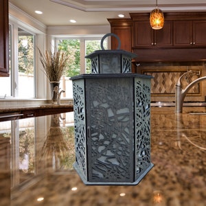 May include: A gray wooden lantern with a decorative cut-out design. The lantern has a hexagonal shape and a handle on the top.