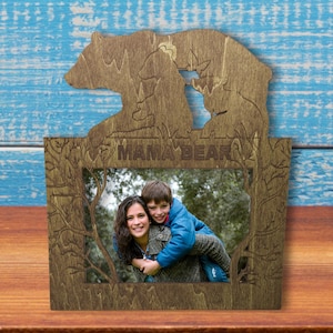 May include: Wooden photo frame with a cutout of two bears, one larger than the other. The frame has the words "Mama Bear" inscribed on it. The frame is holding a photo of a woman and a child.