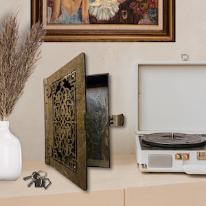 May include: A wooden box with a decorative, intricate, laser-cut design on the front. The box is open, revealing a brown interior. The box is sitting on a wooden surface with a white record player in the background.