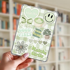 May include: A tablet case with a green and white checkered pattern, adorned with various stickers. Stickers include a heart with "Matcha", a bow, a smiley face, a flower, and the words "Good Vibes" and "Matcha Girlie".