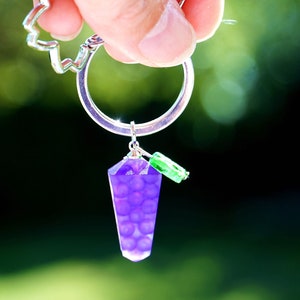 May include: A purple grape charm keychain with a silver key ring and green beads.