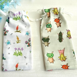 May include: Two small drawstring bags. One is white with a floral pattern of purple, blue, and orange flowers. The other is light green with cartoon characters. Both bags have white drawstrings.