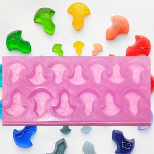 Può includere: Stampo in silicone rosa con 18 cavità a forma di mezzelune con un design a stella all'interno. Lo stampo è circondato da 12 fusioni in resina colorate della stessa forma.
