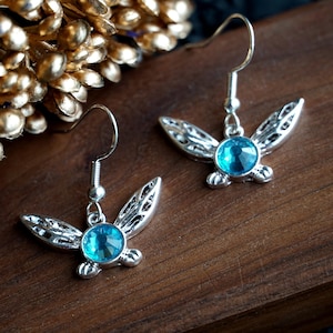 May include: A pair of silver earrings with blue crystal accents. Each earring features a stylised winged design.