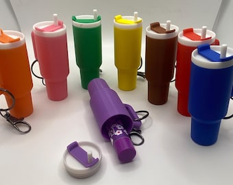 May include: A collection of colorful insulated tumblers with handles and matching lids. The tumblers are in various colors, including orange, pink, green, yellow, brown, red, and blue. A purple lipstick holder and a lipstick are also present.