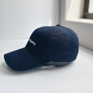 May include: A navy blue baseball cap with a curved peak. The cap has the white text "the reading" embroidered on the front. The hat is made of a soft fabric and has a classic, casual style.