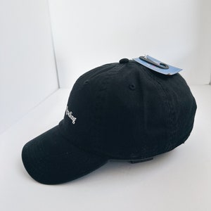 May include: Black baseball cap with a curved peak. The cap features the word "reading" embroidered in white script. A tag is attached to the top of the cap.