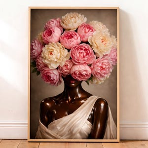 Puede incluir: Una impresión artística enmarcada que presenta a una mujer con piel oscura y una prenda blanca drapeada. Su cabeza es reemplazada por un gran arreglo de peonías rosas y crema. La obra de arte tiene una calidad suave y pictórica, sobre un fondo neutro.