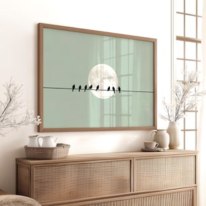 May include: A framed art print featuring a minimalist design of black birds perched on a wire against a pale green background with a large white moon. The artwork is in a wooden frame, suitable for home decor.