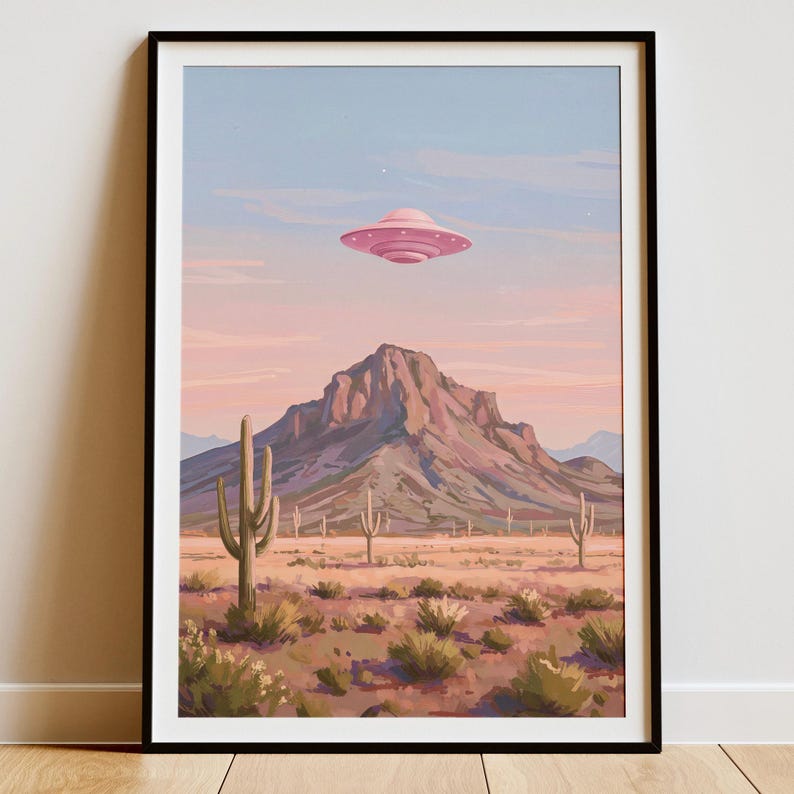 Puede incluir: Impresi&oacute;n art&iacute;stica enmarcada que representa un paisaje des&eacute;rtico con un OVNI rosa flotando sobre una cordillera. La escena incluye cactus, plantas del desierto y un cielo pastel. La obra de arte est&aacute; enmarcada en un marco negro.