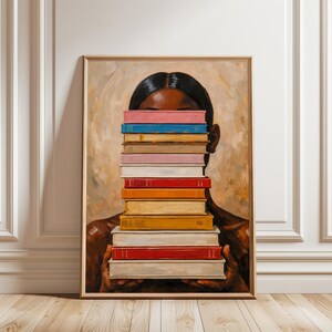Puede incluir: Impresi&oacute;n art&iacute;stica enmarcada que representa a una persona sosteniendo una pila de libros coloridos frente a su rostro. Los libros son de varios colores, incluyendo rosa, azul y rojo. La obra de arte tiene un fondo c&aacute;lido y neutro y un marco de madera.