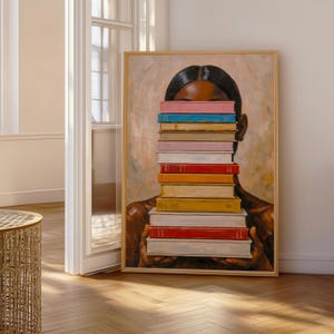 Puede incluir: Una impresi&oacute;n art&iacute;stica enmarcada que representa a una persona sosteniendo una pila de libros coloridos frente a su rostro. Los libros tienen varios colores, incluyendo azul, rosa, naranja y rojo. La obra de arte tiene un fondo c&aacute;lido y neutro.