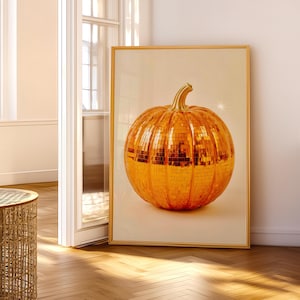 May include: A framed print featuring a large, golden pumpkin with a mosaic-like surface. The pumpkin has a curved stem and is set against a neutral background. The artwork is displayed in a room with natural light.
