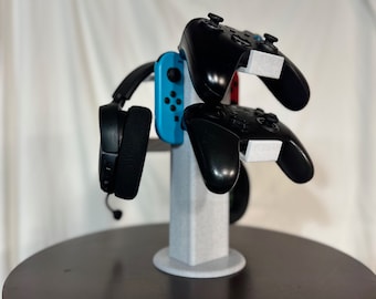 May include: A white stand with a blue and black video game controller, a black headset, and two black video game controllers.