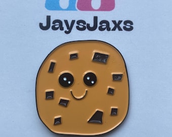 Könnte beinhalten: Ein lächelnder Keks-Emaille-Pin mit Schokoladenstückchen. Der Pin ist hellbraun mit schwarzer Umrandung und schwarzen Schokoladenstückchen-Details. Der Text "JaysJaxs" befindet sich oberhalb und unterhalb des Pins.