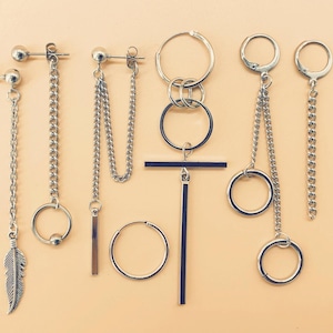 May include: A set of six silver earrings with various chain and hoop designs. The earrings feature a feather charm, a cross charm, and a circle charm.