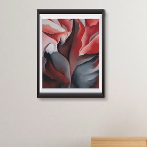 May include: A framed abstract painting with red, gray, and white colors. The painting is hanging on a white wall above a wooden dresser and a pink chair.