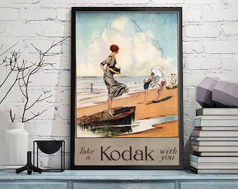 May include: Vintage Kodak advertisement featuring a woman in a striped dress holding a camera on a beach with other people in the background. The text reads "Take a Kodak with you."