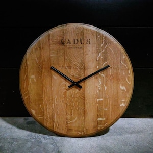 May include: A round wooden clock with black hands, made from a repurposed wine barrel. The clock face features the text "CADUS - FRANCE".