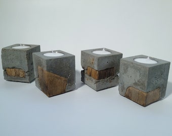 May include: Four concrete candle holders with a rustic wood design. Each holder has a small, round indentation for a tea light candle.