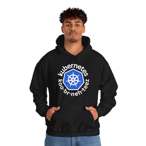 Pode incluir: Moletom preto com capuz e bolso frontal. O moletom apresenta um logotipo Kubernetes branco e azul com o texto "kubernetes koo·br·neh·teez" em um design circular. O moletom é feito de um material macio.